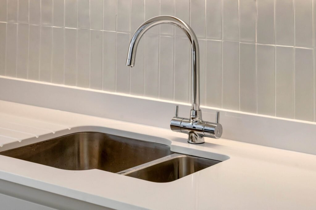 Close-up of stainless steel sink with quartz worktop and decorative tiled splashback